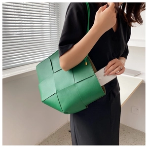 Close-up of green woven leather tote bag showing large Intrecciato pattern and storage
