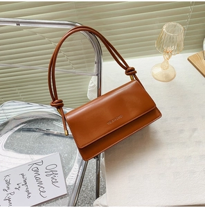 Detailed view of caramel leather baguette bag with knot strap and brand logo display