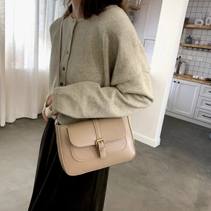 Minimalist apricot flap shoulder bag with gold metal buckle shown in a lifestyle setting