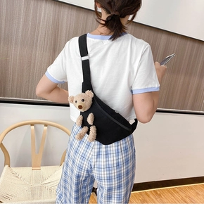 Detailed view of a black canvas chest bag featuring a cute plush bear on a female model