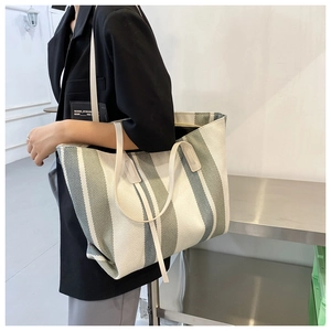 Detailed view of large canvas tote bag with green stripes worn by model on shoulder