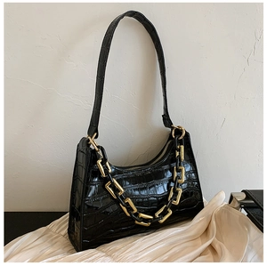 Detailed view of crocodile pattern texture and gold chain on black baguette bag