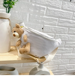 Detail of white canvas chest bag featuring a 3D plush bear and adjustable strap