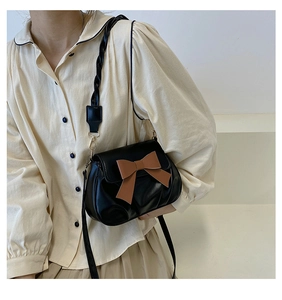 Détail du sac à bandoulière noir avec nœud marron et bandoulière en cuir tressé