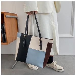 Detail of color-block tote bag showing metal buckles on the handle and rich texture