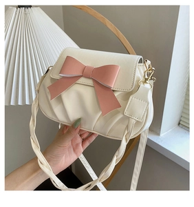 Détail du sac plissé crème avec un nœud en cuir rose et des finitions métalliques dorées