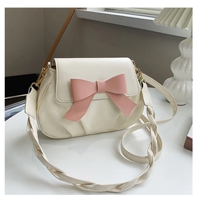 Détail d'un sac bandoulière crème avec un nœud en cuir rose et une bandoulière torsadée