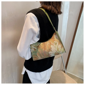 Floral tapestry shoulder bag with green leather strap shown on a model's shoulder