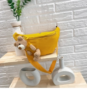 Detail of a ginger yellow canvas chest bag with a cute 3D brown plush bear decoration