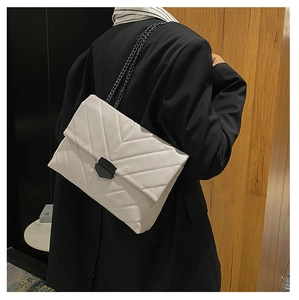 Detail of chevron quilted cream bag with black metal chain strap on black blazer