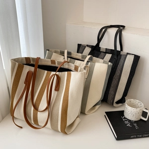 Minimalist striped canvas tote bags in brown, green, and black displayed on a white table