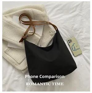 Détail du sac hobo en nylon noir avec bandoulière en cuir à côté d'un téléphone portable