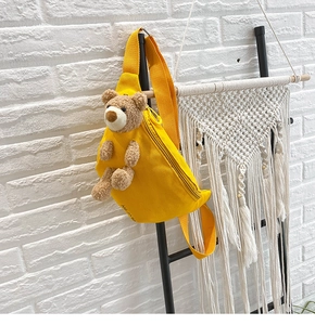 Detail of a bright yellow canvas chest bag featuring a cute 3D plush bear mascot decor