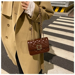 Close-up of a quilted dark brown crossbody bag with gold chain strap on a camel coat