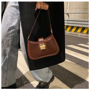 Chic dark brown faux leather crescent bag with a gold metal buckle on a street backdrop
