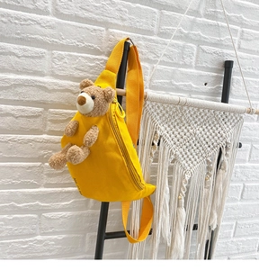 Detail of yellow canvas chest bag featuring a 3D plush teddy bear and adjustable strap