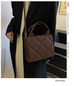 Detail of dark brown quilted leather square handbag with golden hardware and round handle