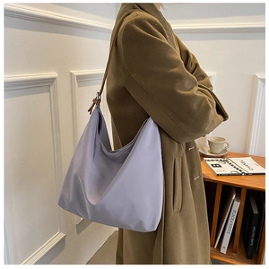 Détail d'un sac hobo lilas porté avec un manteau beige dans un décor minimaliste chic