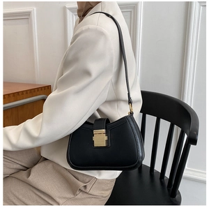Detail shot of a minimalist black leather underarm bag with an elegant golden clasp