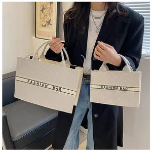 Détail de deux sacs cabas en toile crème avec jacquard de lettres et broderie
