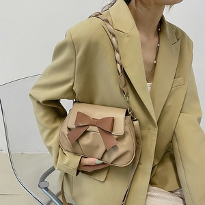 Sac bandoulière beige chic avec nœud marron et bandoulière tressée porté par un mannequin