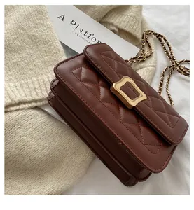 Detail of brown quilted leather bag with gold buckle on beige sweater background