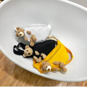 Detailed view of canvas chest bags in white, black and yellow with plush bear ornament