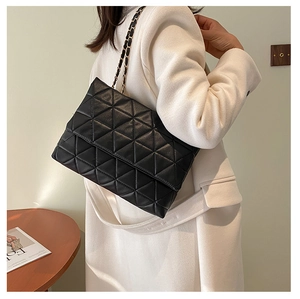 Gros plan d'un sac bandoulière matelassé noir avec chaîne porté par un mannequin