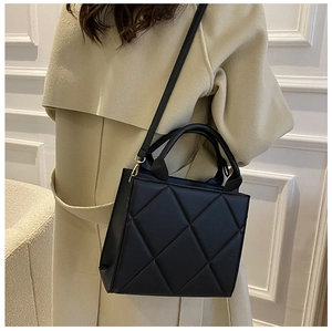 Detail of a black quilted leather square handbag with gold-tone metal buckles on a model
