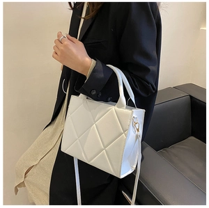 Close-up of a white quilted crossbody bag with diamond stitching held by a model
