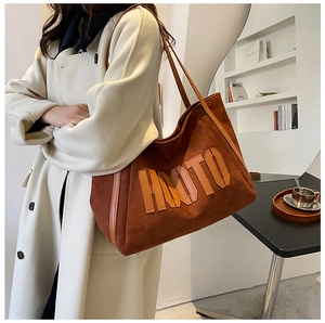 Detail of suede tote bag in brick red featuring large embossed HMOTO letters on the side