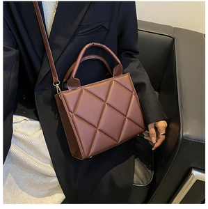 Detail of a brown quilted crossbody bag featuring elegant faux leather texture and top handle