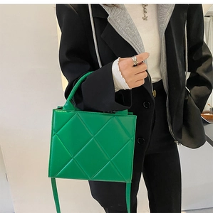 Detailed shot of green quilted small square bag with crossbody strap and handle