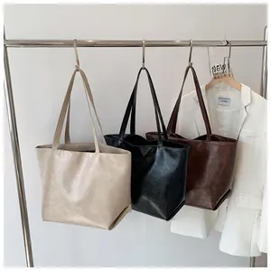 Trois sacs cabas minimalistes en crème, noir et marron suspendus sur un portant en métal