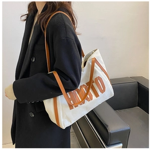 Detail of canvas tote bag with brown leather trim and embossed HODTO lettering on a model