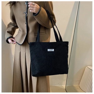 Détail du grand sac cabas en velours côtelé noir porté à l'épaule par un mannequin