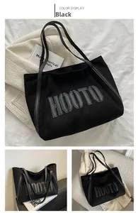 Detail of black suede tote bag with HOOTO letter patch and slim synthetic leather straps