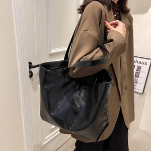 Grand sac cabas noir minimaliste en cuir brillant porté avec un blazer marron chic