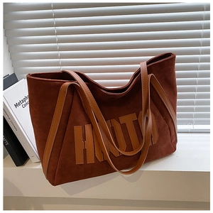 Detail of brown faux suede tote bag featuring large letter embroidery and leather handles