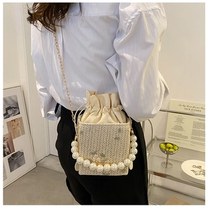 Detail of woven straw box bag featuring pearl top handle and elegant floral embroidery