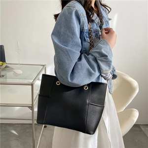 Grand sac cabas noir en cuir avec chaîne dorée porté par un mannequin en studio