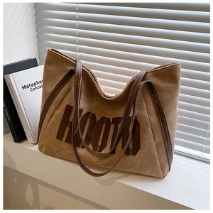 Detail of suede tote bag featuring contrast lettering and fine stitching on handles