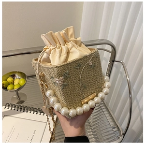 Detail of woven straw bucket bag featuring floral embroidery and large pearl handle