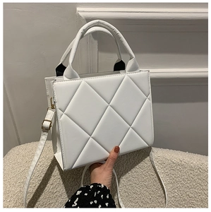 Close-up of white quilted faux leather bag featuring top handles and adjustable strap