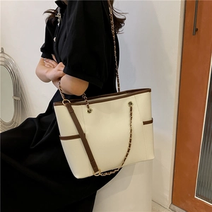 Sac cabas beige élégant avec anses marron et chaîne dorée porté par un mannequin