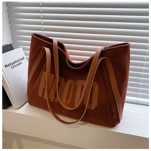 Close-up of caramel suede tote bag featuring large letter appliqué and slim leather strap