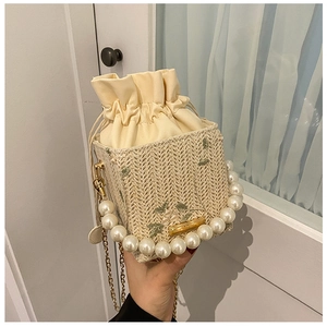 Detail of woven straw bucket bag featuring green floral embroidery and pearl handle