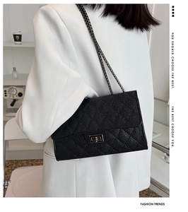 Detail of black quilted leather crossbody bag with silver twist lock on white blazer