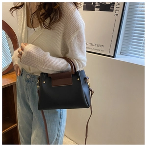 Detail of a two-tone Boston bag showing adjustable brown shoulder strap and metal D-rings