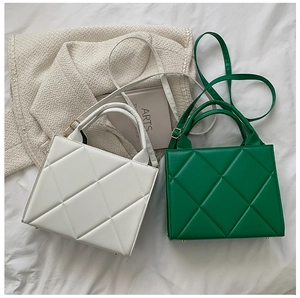 Flat lay of green and white quilted square handbags with top handles and adjustable straps